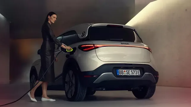 Ein weißer smart #1 wird von einer Frau in einem dunklen Kostüm geladen.