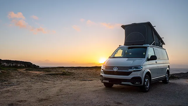 Camping mit dem VW California im Sonnenuntergang und aufgestelltem Dach.