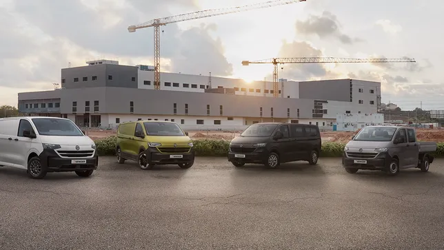 Vier Volkswagen Nutzfahrzeuge Transporter Modelle auf einem Parkplatz mit einer Baustelle im Hintergrund.