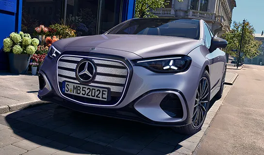 Eine perlmuttfarbene elektrische Mercedes-Benz C-Klasse steht auf einem Parkplatz auf der Straße vor einem Geschäft mit blauer Front.