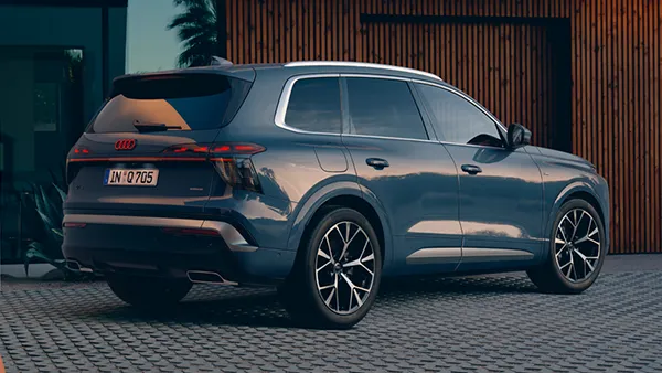 Heckansicht eines Audi Q7 mit markantem Hecklichtband und schwarzem Dachspoiler vor einer Holzfassade.