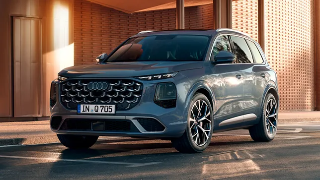 Blaue Audi Q7 Frontansicht mit markantem Kühlergrill und LED-Scheinwerfern vor einer modernen Backsteinwand.