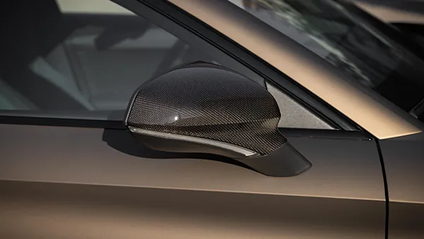 Seitlicher Außenspiegel eines CUPRA Leon Sportstourer mit glänzender Carbon-Oberfläche und bronzefarbenem Lack am Türrahmen.