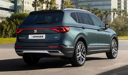 Ein grauer SEAT Tarraco steht auf einer Straße mit Palmen und Gebäuden im Hintergrund.