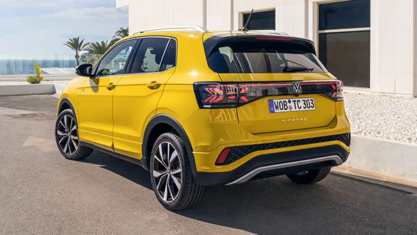 Gelber VW T-Cross von hinten mit schwarzem Dach und markanten Rückleuchten vor modernem Gebäude.