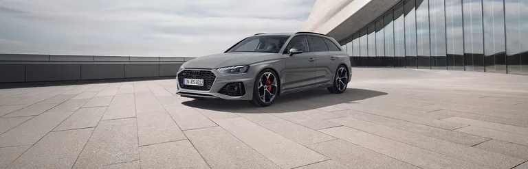 Seitenansicht eines grauen Audi RS 4 auf gepflastertem Platz vor einem modernen Glasgebäude
