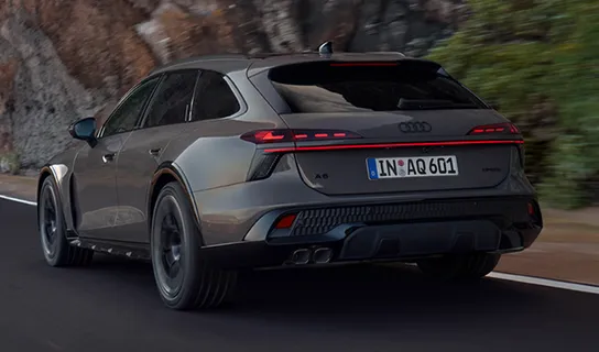 Ein dunkelgrauer Audi A6 allroad fährt auf einer Straße vor Felswand entlang.