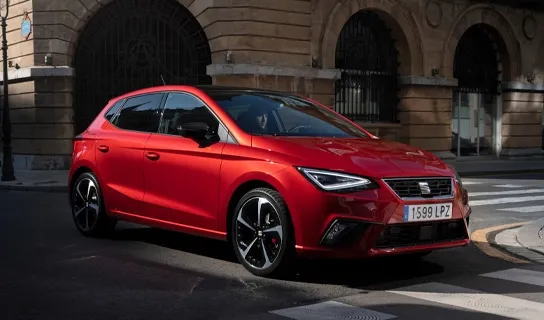 Ein roter SEAT Ibiza steht vor einem Zebrastreifen vor einem historischen Gebäude, daneben geht eine Personen über einen weiteren Zebrastreifen.