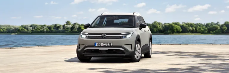 Ein hellgrauer VW ID. Cross steht auf einem Platz vor einem See mit bewaldetem Ufer im Hintergrund.