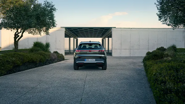 Ein VW ID. Cross in grün metallic steht vor einem modernen, weißen Gebäude mit zwei Bäumen und Büschen links und rechts.