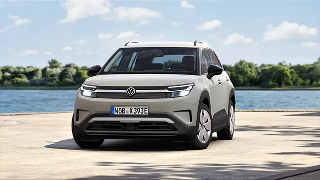 Ein hellgrauer VW ID. Cross steht auf einem Platz vor einem See mit bewaldetem Ufer im Hintergrund.