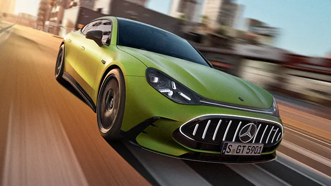 Ein grünes Mercedes AMG GT 4-Türer Coupé fährt auf einer Straße in urbaner Umgebung bei Sonnenuntergang