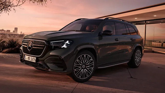 Ein chwarzer Mercedes GLS mit markantem Kühlergrill und großen Felgen steht vor einem modernem Gebäude mit Glasfront bei Sonnenuntergang