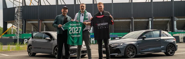 Drei Männer stehen vor zwei grauen Autos mit Senger-Logo, im Hintergrund ist ein Stadion zu sehen. Der linke und der mittlere Mann halte ein grünes SC Preußen Münster-Trikot mit der Aufschrift 'Münster 2027 Senger', der rechte ein schwarzes Senger-Trikot.