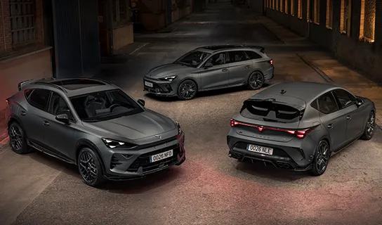 Ein grauer CUPRA Formentor VZ5, CUPRA Leon Sportstourer VZ und CUPRA Leon VZ mit eingeschalteten LED-Scheinwerfern und -Heckleuchten stehen in einer dunklen, schmalen Gasse mit Backsteinwänden.