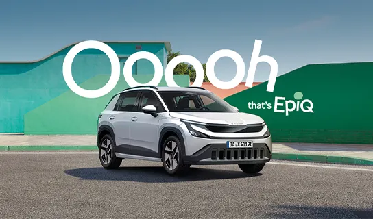 Ein weißer Škoda Epiq steht auf einem Parkplatz vor einer grünen Wand. Hinter dem Fahrzeug steht die Aufschrift 'Ooooh that's Epiq'.