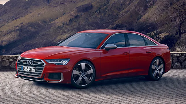 Eine rote Audi S6 Limousine steht auf einem gepflasterten Platz mit Steinmauer vor einer Berglandschaft.