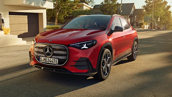 Ein roter Mercedes-Benz elektrischer GLA steht auf einer sonnigen Wohnstraße mit herbstlichen Bäumen und modernen Häusern im Hintergrund.